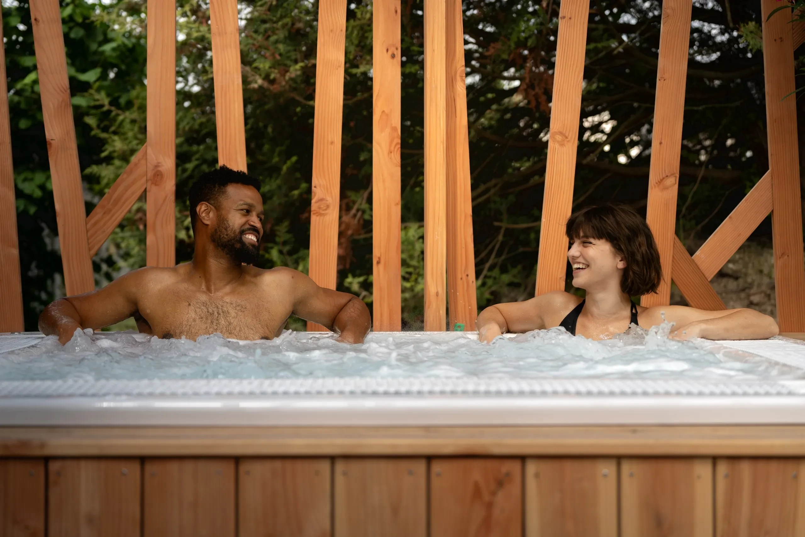 Deux personnes sourient dans un jacuzzi extérieur.